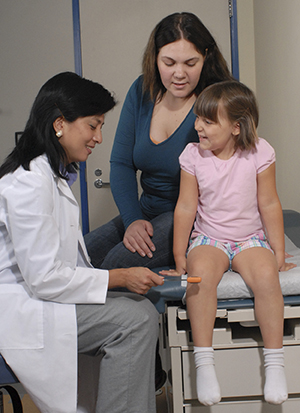 Health care provider testing girl's knee reflex in exam room.